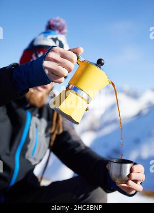 Man hiker pouring coffee from Yellow Moka mocha pot outdoors in the snow winter mountains. Old style coffee vintage pot outdoor camping Stock Photo