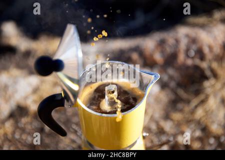 Yellow Moka coffee pot on stove on table with open cover with brown hot beverage splash drop. Old style coffee vintage pot outdoor camping Stock Photo