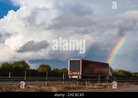 Refrigerated semi-trailer truck driving on a highway under a rainbow. Stock Photo