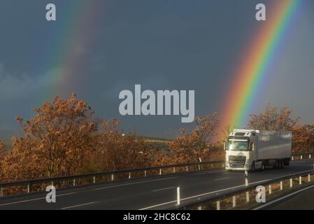 Refrigerated semi-trailer truck driving on a highway under a rainbow. Stock Photo