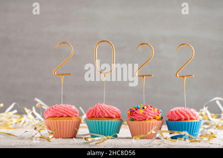 New year cupcakes and gold sparklers numbers 2022. Holiday muffins with pink buttercream frosting. Gray background Stock Photo