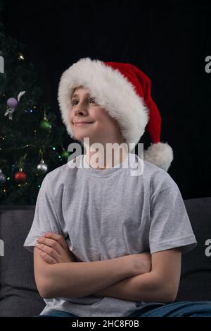 Portrait of teenage boy in Santa hat in dark key. Vertical frame. Stock Photo