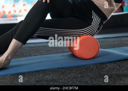 Fitness woman massages thigh muscles with a fascia roller outdoors ...