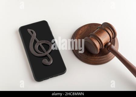 Mobile phone with treble clef sign on display and judges hammer. Illegal use of music concept. Digital piracy Stock Photo