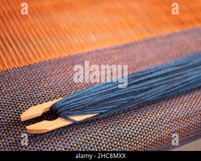 Weaving shuttle with blue thread on the orange warp, close up Stock Photo