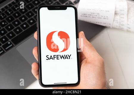 Safeway application on the screen of Apple iPhone in mans hand and laptop on the background. Online shopping concept. November 2021, San Francisco, USA Stock Photo