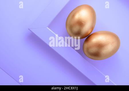 Golden colored Easter eggs on a purple background for spring project, violet colour of the year 2022. Stock Photo