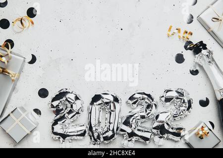 New Year 2022 gray background flat lay. Top view on 2022 balloon silver metallic numbers with confetti, grey gift boxes. Invitation or greeting card concept. Festive mood. Bottle of champagne bottle Stock Photo