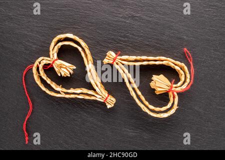 Two Christmas toys made of straw in the shape of a heart on a slate stone, close-up, top view. Stock Photo