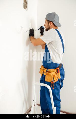 Concentrated electrician, handyman using screwdriver while working on installing socket on wall at home Stock Photo