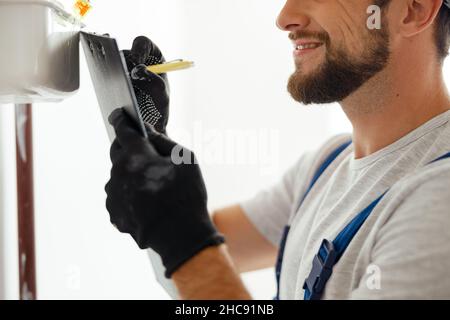 Side view of heating fitter in protective gloves making notes while checking gas consumption at gas pipe and meter counter Stock Photo