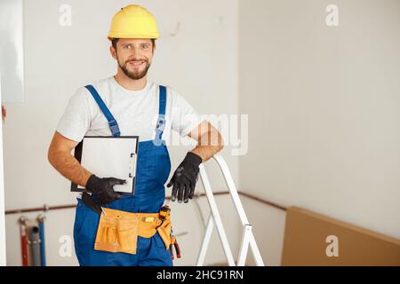 Smiling repairman holding clipboard and smiling at camera while standing in new apartment Stock Photo