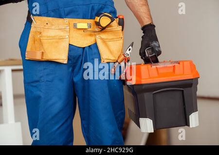 Closeup shot of contractor worker in overalls holding toolbox while standing indoors Stock Photo