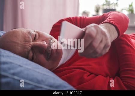 Senior caucasian man using smart phone lying on sofa at home. Stock Photo