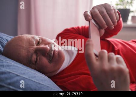 Senior caucasian man using smart phone lying on sofa at home. Stock Photo