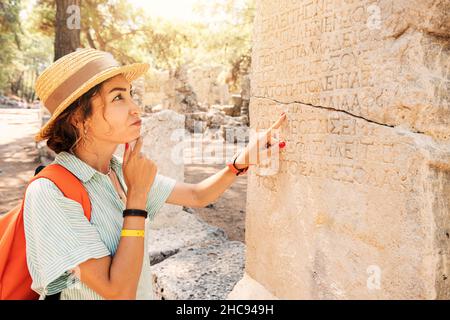 Woman philologist and tourist reads and tries to translate ancient Greek from columns in the ruins of an antique city. Linguistics and archaeology Stock Photo