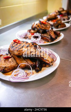 BBQ grill ribs served in portions in the restaurant kitchen. Plates with meat dish close-up. Stock Photo