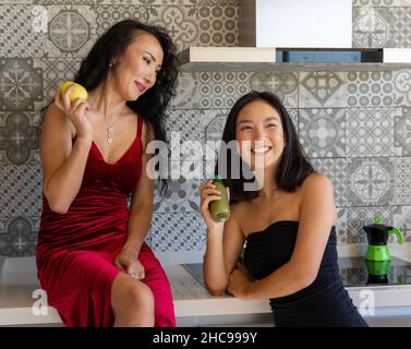 two women enjoying their time having a snack in the kitchen, well-dressed in formal clothes Stock Photo