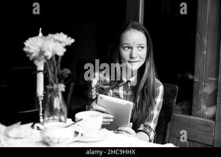Girl sits with a tablet in an outdoor cafe. Black and white photo. Stock Photo