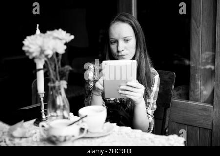 A girl sits with a tablet in an outdoor city cafe. Black and white photo. Stock Photo