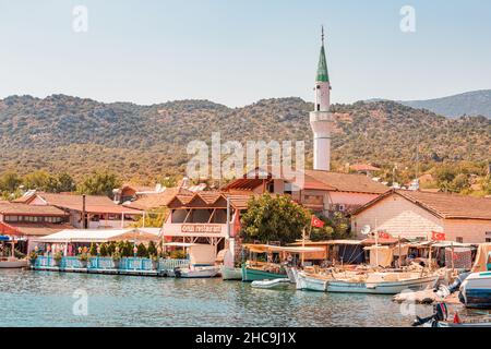 28 August 2021, Kaleucagiz, Turkey: Coastal town with fishing boats, cafe and mosque minaret Stock Photo