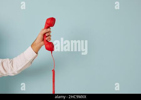 Unidentified man holding red wired retro telephone handset on light blue banner background. Stock Photo