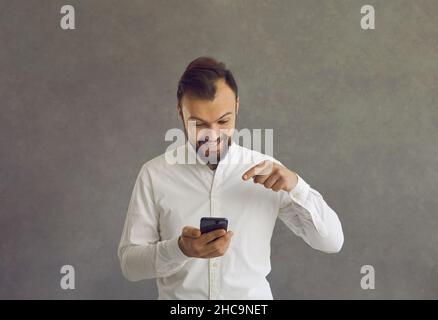 Happy smiling excited man holding smartphone pointing to mobile screen Stock Photo