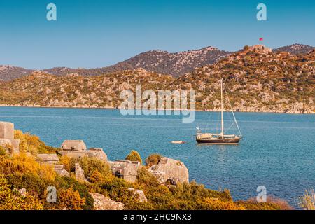 Yacht and boat tours to the sunken town of Kekova in Turkey against the background of ancient castle Simena on a high rock with Turkish flag Stock Photo