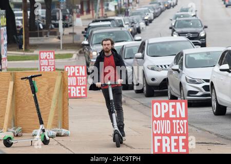 Austin, Texas, USA. 26th December, 2021. A man on a scooter flies past a mobile private COVID testing site overwhelmed by residents wanting to get tested during the holidays. Patrons reported up to two-hour waits at the drive-through site, one of several opened over the Christmas holidays. Credit: Bob Daemmrich/Alamy Live News Stock Photo