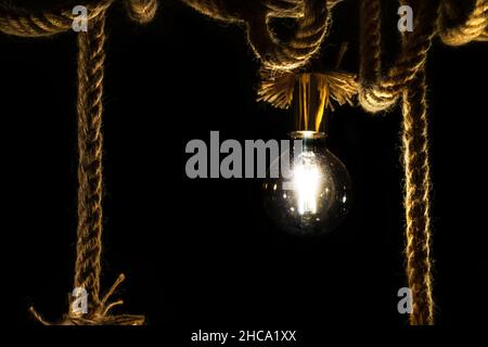 Old light bulb on rope in front of black background Stock Photo