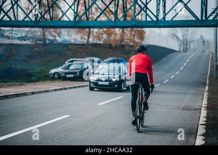 A back view of a young cool male cyclist in red sportswear riding a bicycle on a gloomy day Stock Photo