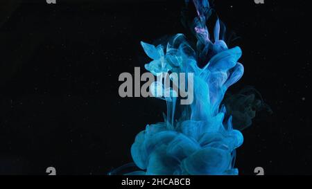 Blue paint drops mixing in water slow motion. Smooth ink swirling and splashing from above underwater leaving ink cloud on black background. Stock Photo