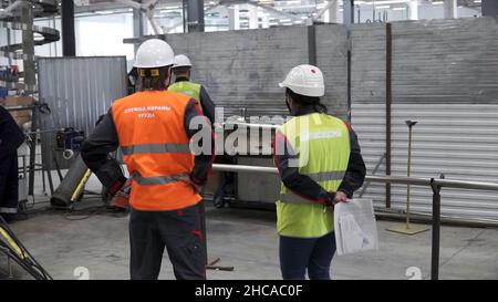 Rear view of workers talking while walking in shipping yard. Back view of two men in white safety hard hats are standing together in construction area Stock Photo