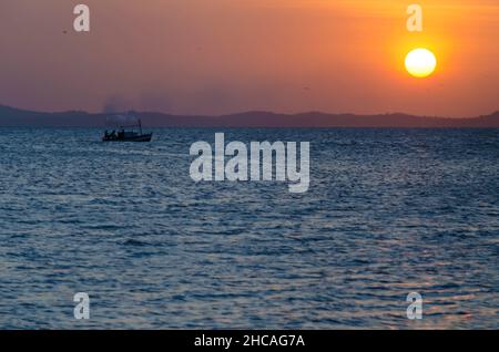 Sunset seen from Ribeira beach in Salvador, Bahia, Brazil. A boat sails at sea. Stock Photo