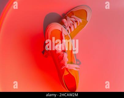 Trendy fashion white sneakers on abstract bright background. Neon lights on casual shoes. Orange and red gradient light. Minimalism, 90s concept. Stock Photo