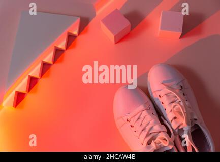 Trendy fashion white sneakers on abstract bright background. Neon lights on casual shoes. Orange and red gradient light. Minimalism, 90s concept. Stock Photo