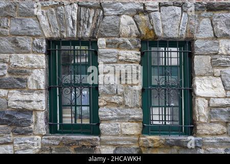 Rough stone wall of an old building with arched barred windows in hard ...