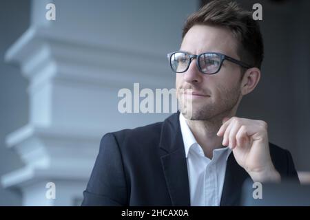Confident attractive young businessman sitting at home office, looking aside with pensive expression Stock Photo