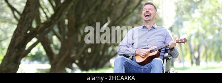 Man in wheelchair plays guitar in park and makes money Stock Photo
