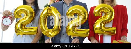 Group of business people in santa claus hats holding golden balloons with numbers 2022 near new year tree Stock Photo
