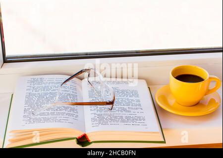 an open book with reading glasses and a cup of strong coffee on the windowsill. the concept of reading your favorite book Stock Photo