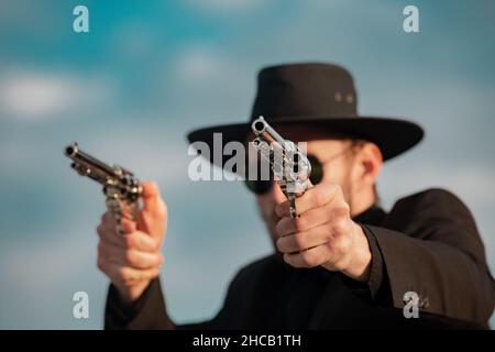 Sheriff in black suit and cowboy hat shooting gun, close up western portrait. Wild west, western, man with vintage pistol revolver and marshal Stock Photo