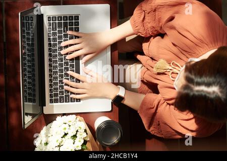 Female software developer working on laptop and drinking coffee in disposable cup, view from the top Stock Photo
