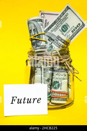 Glass jars filled with dollar bills, savings inside glass jar, money isolated on yellow background. Paper note written word FUTURE. Business budget of Stock Photo