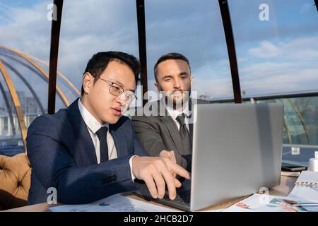Confident Chinese businessman pointing at screen of laptop during discussion of online data or document Stock Photo
