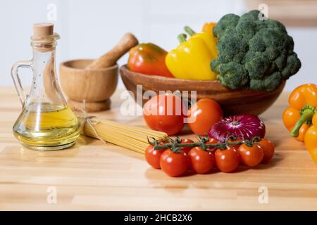 Group of fresh ripe tomatoes, peppers, and broccoli, bottle of olive oil and bunch of spaghetti on kitchen table Stock Photo