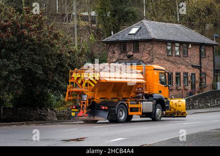 Orange winter maintenance gritter salt spreading lorry with snow plough fitted treating road surface before freezing temperatures to prevent ice form Stock Photo