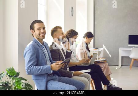 Happy man using tablet computer while waiting in line with other business people Stock Photo