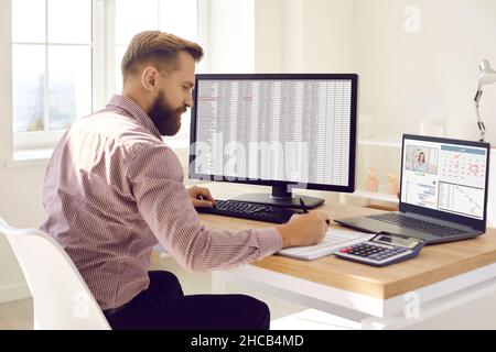 Accountant multitasking while working with data on computers at his desk in office Stock Photo