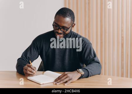 Young african american man entrepreneur in glasses taking notes in agenda Stock Photo